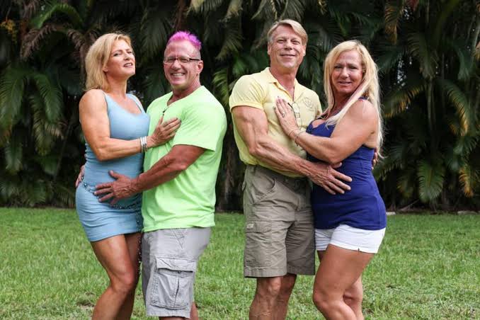 Two couples posing together outdoors in front of palm trees representing mature swingers